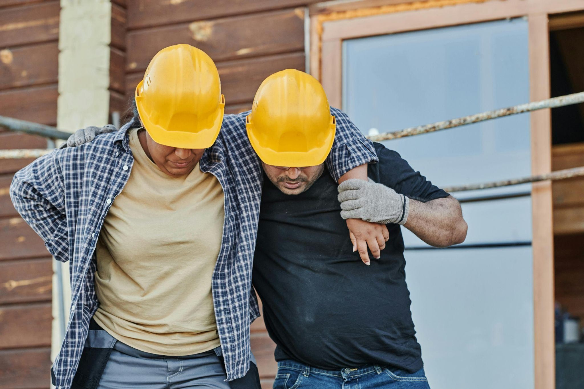 A construction worker with a hand on her lower back is helped to walk by a colleague at a site, representing a workplace injury and workers' comp claim.