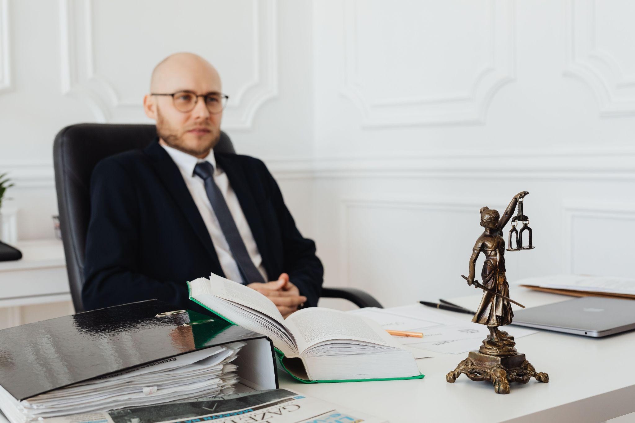 Attorney sitting at a desk with legal documents and Lady Justice statue, discussing the benefits of a revocable living trust.